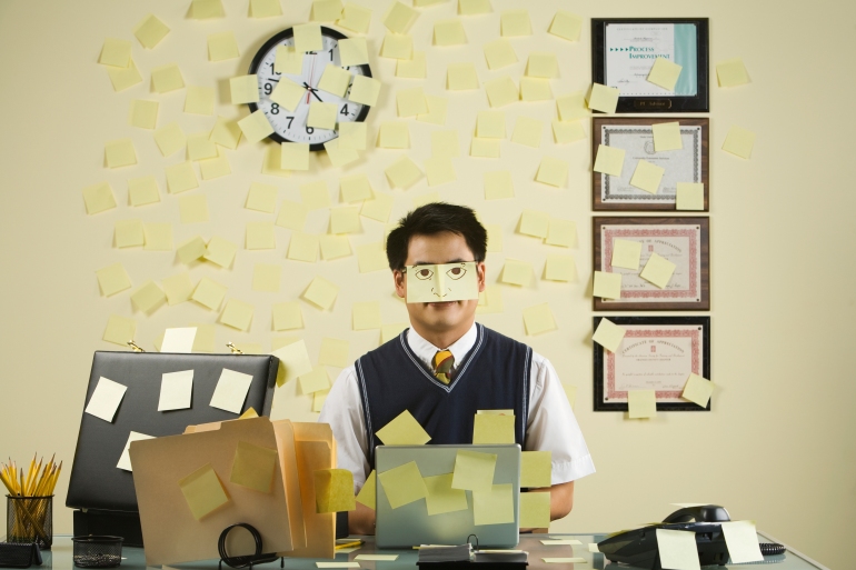 Asian businessman with sticky notes all over wall and face - stock photo