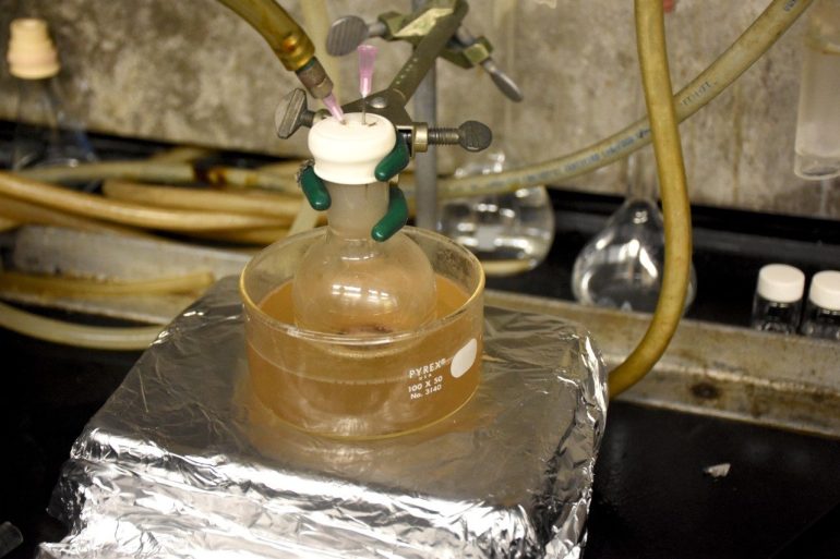 A flask filled with waxes generated from waste polyethylene and polypropylene is heated in an oil bath, and the waxes are oxidized by a stream of airflow to produce fatty acids via catalytic oxidation. Photo by Steven Mackay for Virginia Tech.