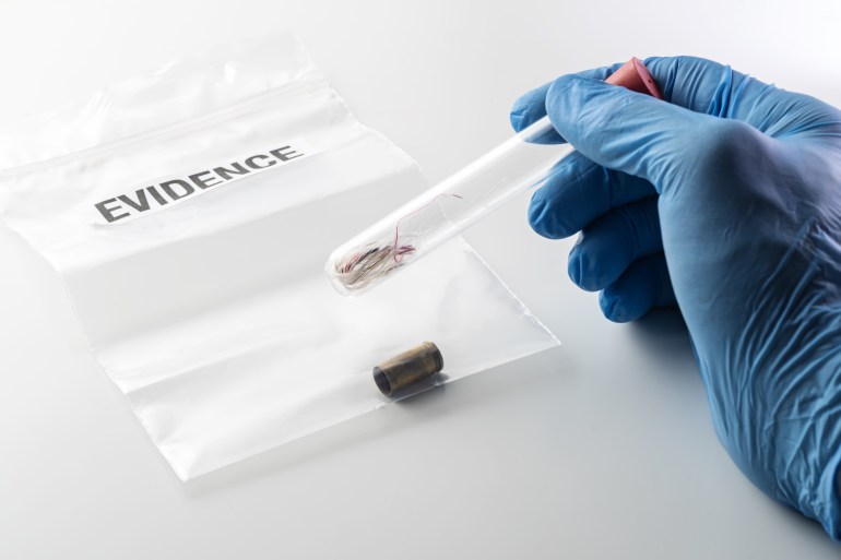 Closeup of forensic scientist's hand in blue rubber glove holding glass tube over evidence bag with 9 mm bullet case. Crime, forensic science, investigation and violence concepts.