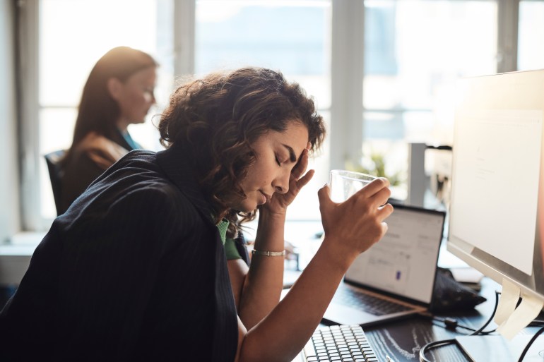 Tired businesswoman with head in hand holding drinking glass at office