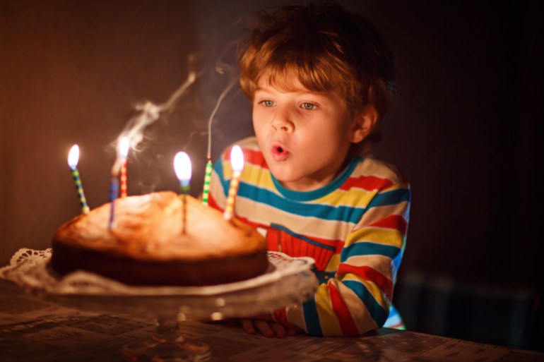 Happy little kid boy celebrating his birthday and blowing candles on homemade baked cake, indoor. Birthday party for children. Carefree childhood, anniversary, happiness. Five years old