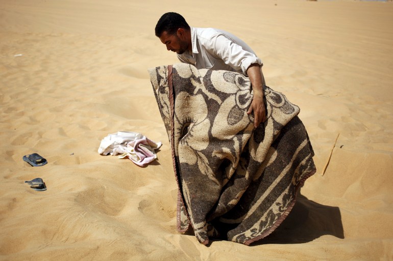 A worker helps a patient, who is wrapped in a blanket, leave a "sauna" tent after his sand bath in Siwa, Egypt, August 12, 2015. In the searing heat of summer in western Egypt, at the hottest time of the day, sufferers of rheumatism, joint pain, infertility or impotence lie buried neck-deep in the sand of Siwa near Dakrour Mountain. Locals say taking a sand bath is a natural therapy with powers to cure many medical conditions. Patients relax in the shade before treatment, which includes massages by the feet of health workers after they submerge their patients up to their neck in the desert. Patients drink mint tea in tents following the treatment. REUTERS/Asmaa Waguih PICTURE 20 OF 24 FOR WIDER IMAGE STORY "THE HOT SAND BATHS OF SIWA". SEARCH "ASMAA SIWA" FOR ALL IMAGES