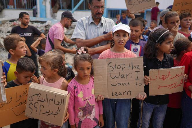 شباب فلسطينيون يحملون لافتات تطالب بإنهاء النزاع في غزة واستئناف الدراسة قبل العام الدراسي الجديد، بجوار مبنى مدرسي متضرر في خان يونس، جنوب قطاع غزة، في 28 أغسطس 2024.