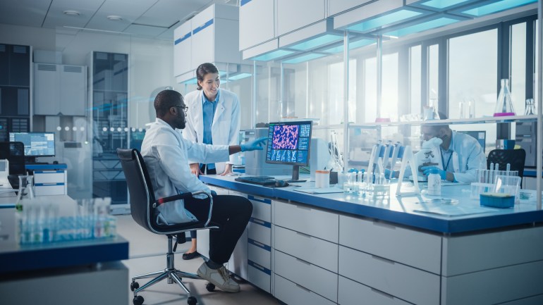 Modern Medical Research Laboratory: Two Scientists Use Computer with Screen Showing DNA Gene Analysis, Specialists Discuss Innovative Technology. Advanced Scientific Lab for Medicine, Biotechnology