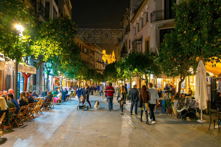 Seville, Spain - December 9 2023: The lights of the Seville Cathedral in the distance from a busy touristic ...