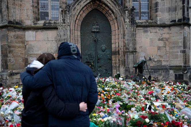 زوجان يتعانقان أمام الزهور والشموع التي تركت أمام كنيسة يوهانيس، بالقرب من سوق عيد الميلاد حيث قادت سيارة وسط الحشد مساء الجمعة، في ماغديبورغ، ألمانيا، 22 ديسمبر 2024. 