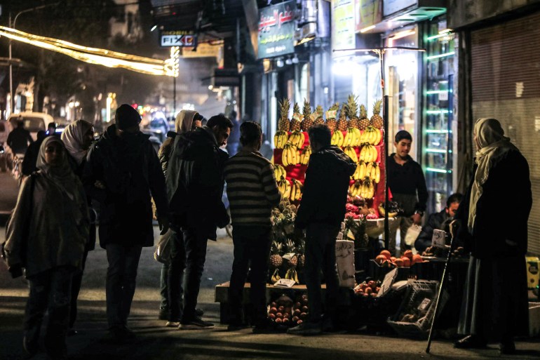 Men browse bananas, pinaepples, and other fruit on display at a vendor's stall along a street in Damascus on December 18, 2024. - Islamist-led rebels took Damascus in a lightning offensive on December 8, ousting president Bashar al-Assad and ending five decades of Baath rule in Syria. (Photo by Bakr ALKASEM / AFP)