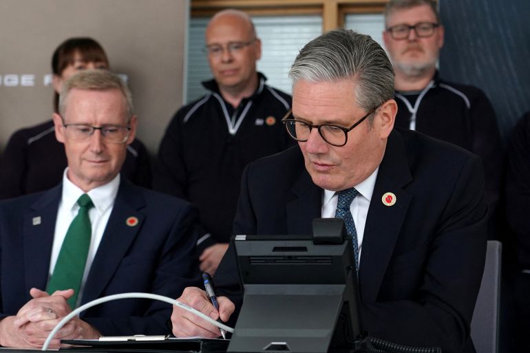Britain's Prime Minister Keir Starmer makes notes as he discusses over the phone a UK-US trade deal with US President Donald Trump at a car factory in the West Midlands, central England on May 8, 2025. (Photo by Alberto Pezzali / POOL / AFP)