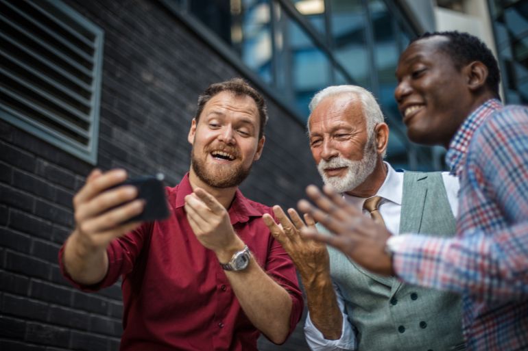 Three business men standing outside and using mobile phone.