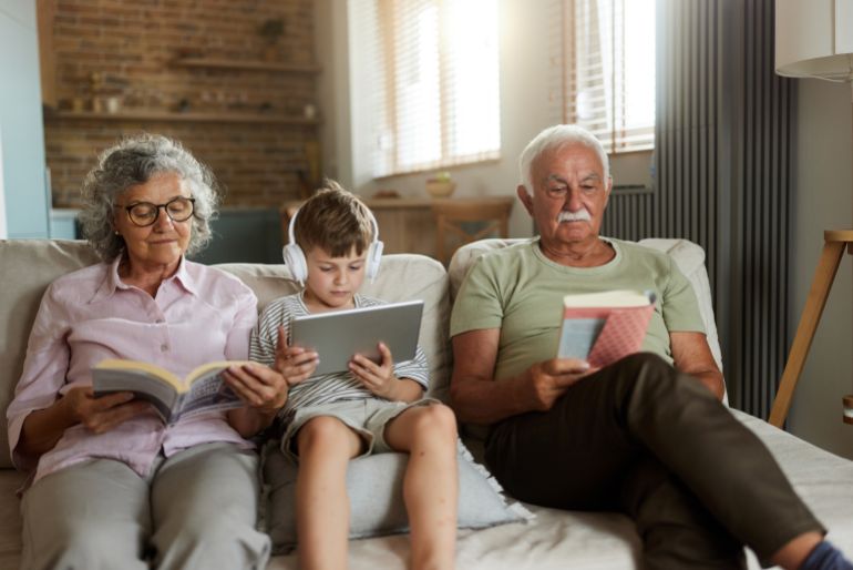 Mature grandparents reading books while their small grandson is using digital tablet at home.