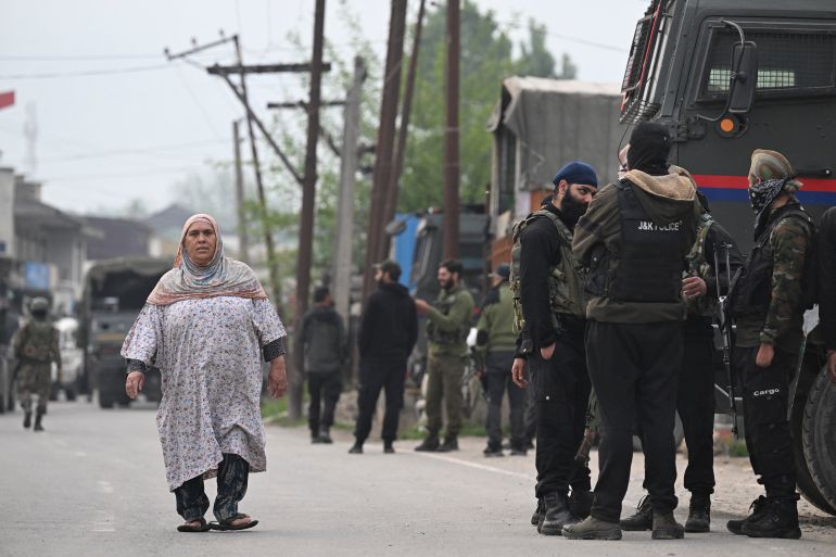 Indian security personnel stand guard as a woman walks along a road in Wuyan near Indian-administered Kashmir's main city of Srinagar on May 7, 2025.