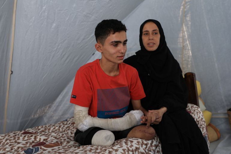 Ahmad Al-Ghalban, a 16-year-old Palestinian gymnast, who lost both his legs in an Israeli airstrike on Beit Lahiya, sits on his bed beside his mother inside the tent they took shelter in, after being displaced, in Gaza City, May 21, 2025. REUTERS/Dawoud Abu Alkas