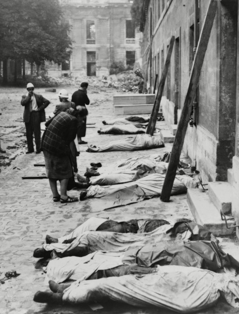 أصدقاء وأقارب يبحثون عن جثث مقاتلي قوات الداخلية الفرنسية (FFI). جثثهم ملفوفة بملاءات، مصفوفة على جانب مبنى، ربما في <a class=