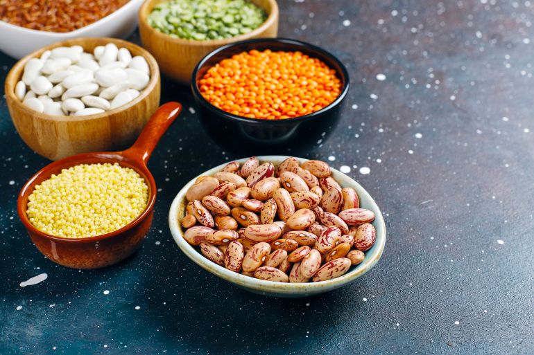 Legumes and beans assortment in different bowls on light stone background