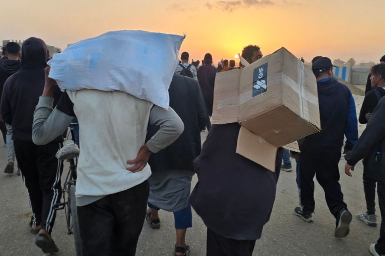 A youth carries an empty box of relief supplies from the Gaza Humanitarian Foundation (GHF), a private US-backed aid group that has bypassed the longstanding UN-led system in the territory, as displaced Palestinians walk near a food distribution centre in Rafah in the southern Gaza Strip on June 1, 2025. Gaza rescuers said Israeli gunfire killed at least 10 Palestinians and wounded more than 100 early on June 1, as thousands of people headed towards a US-backed aid distribution site. (Photo by AFP)