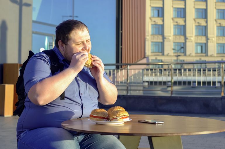 Male office worker eating burger for lunch outdoors, junk food nutrition obesity
