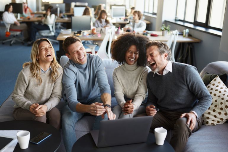Team of cheerful diverse entrepreneurs laughing while working on a computer in the office.
