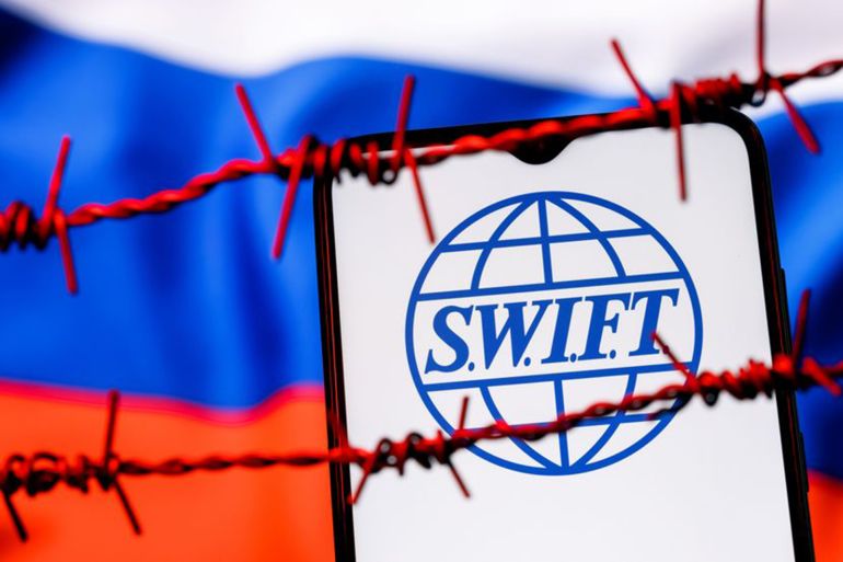 Kazan, Russia - Feb 25, 2022: SWIFT financial system logo on smartphone screen behind barbed wire on background of Russian flag. Sanctions against Russia, disconnection from SWIFT.