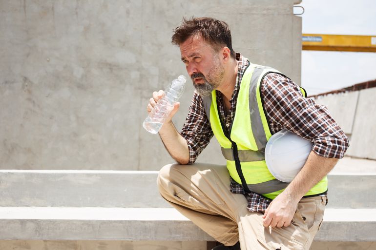 Dangerous from heat wave during working outside the building. Caucasian male construction worker resting and drinking water from bottle in a very hot day. Heat stroke health problem.; Shutterstock ID 2462479271; purchase_order: aj; job: ; client: ; other: