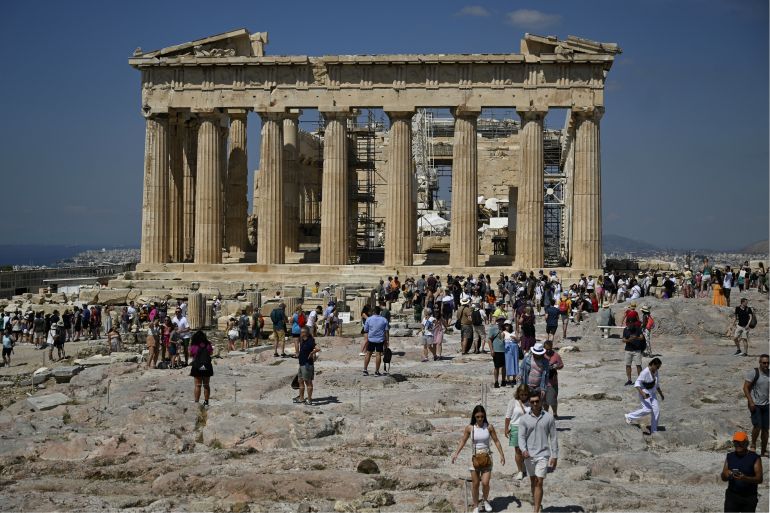 (FILES) Tourists walk in front of the Parthenon Temple as they visit the Acropolis archaeological site in Athens on June 14, 2023. (Photo by Louisa GOULIAMAKI / AFP)