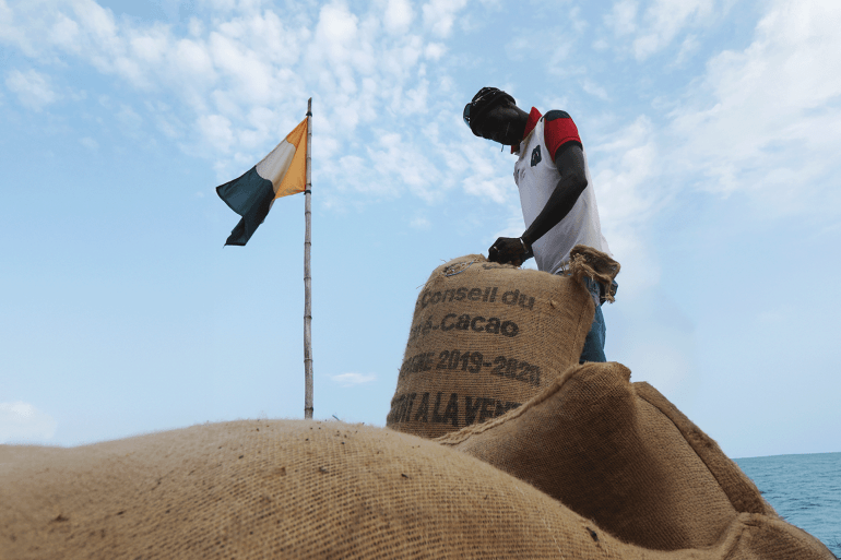 A worker sews up cocoa sacks next to an Ivory Coast flag in Soubre, Ivory Coast January 7, 2021. Picture taken January 7, 2021. REUTERS/Luc Gnago