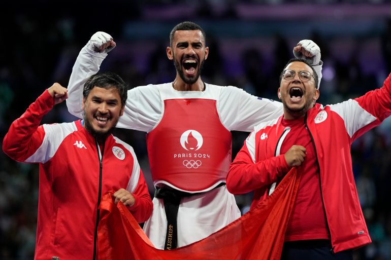 Tunisia's Firas Katoussi, right, celebrates with his coaches after winning the gold medal in a men's 80kg Taekwondo final match against Iran's Mehran Barkhordari during the 2024 Summer Olympics, at the Grand Palais, Friday, Aug. 9, 2024, in Paris, France. (AP Photo/Andrew Medichini)