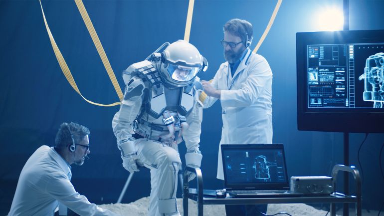 Astronaut and scientists preparing for zero gravity test - stock photo Medium shot of scientists adjusting anti-gravity bands on astronauts spacesuit for a low gravity test
