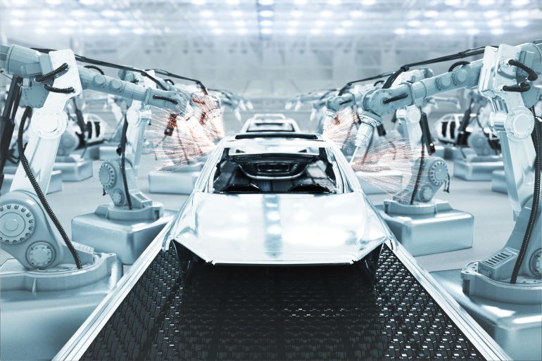 Robotic arm welding the car in a futuristic assembly automotive manufacturing plant.