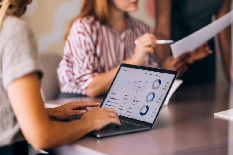 A group of professionals engaged in a business meeting, focused on data analysis displayed on a laptop screen. Charts and graphs indicate an analytical approach to teamwork and collaboration.