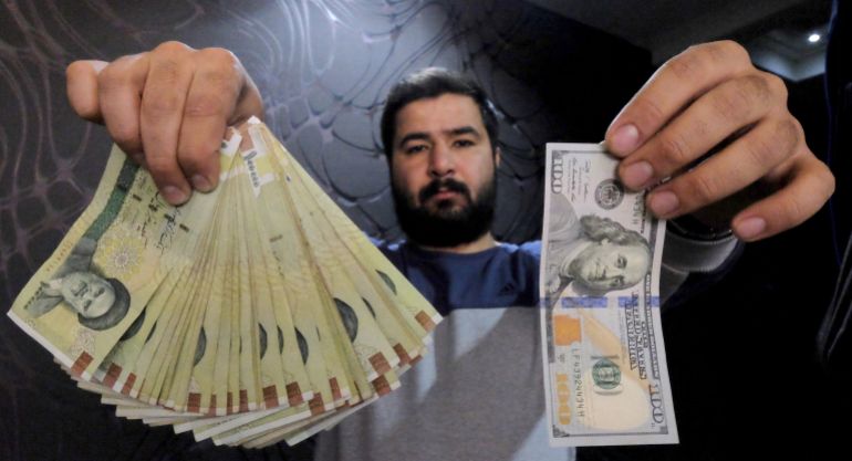A money changer poses for the camera with a U.S hundred dollar bill (R) and the amount being given when converting it into Iranian rials (L), at a currency exchange shop in Tehran's business district, Iran, January 20, 2016. REUTERS/Raheb Homavandi/TIMA ATTENTION EDITORS - THIS IMAGE WAS PROVIDED BY A THIRD PARTY. FOR EDITORIAL USE ONLY.