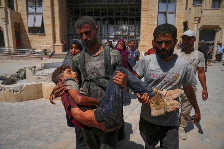 A Palestinian carries the body of a youth killed while trying to reach trucks carrying humanitarian aid en route to Gaza City, outside the Hamad Al-Qatari Hospital in Beit Lahiya, northern Gaza Strip, Friday, Aug. 1, 2025. (AP Photo/Jehad Alshrafi)