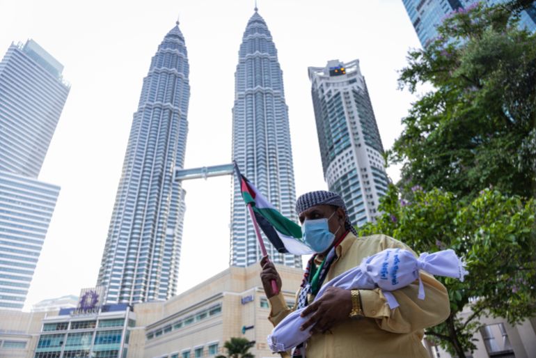 KUALA LUMPUR, MALAYSIA - AUGUST 02: A pro-Palestinian protester holds a Palestinian flag and a mock body bag in front of the Petronas Twin Towers during a march to express solidarity with the people of Palestine on August 2, 2025 in Kuala Lumpur, Malaysia. Protesters in Malaysia joined marches and actions globally, as pressure mounts on the Israeli government over a devastating humanitarian crisis unfolding as its war against Hamas continues. (Photo by Annice Lyn/Getty Images)