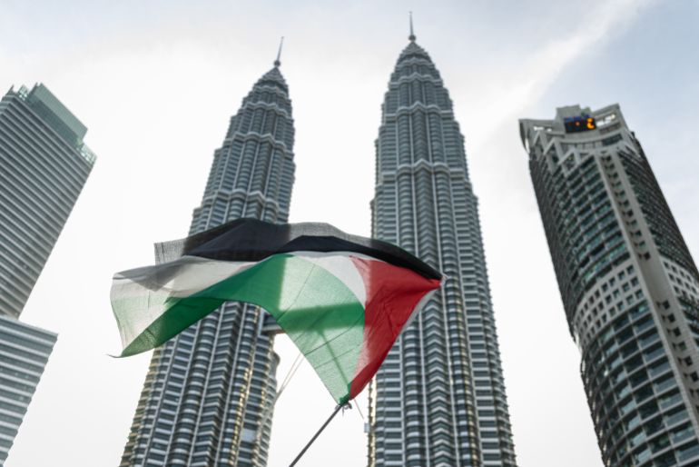 KUALA LUMPUR, MALAYSIA - AUGUST 02: A pro-Palestinian protester waves a Palestinian flag in front of the Petronas Twin Towers during a march to express solidarity with the people of Palestine on August 2, 2025 in Kuala Lumpur, Malaysia. Protesters in Malaysia joined marches and actions globally, as pressure mounts on the Israeli government over a devastating humanitarian crisis unfolding as its war against Hamas continues. (Photo by Annice Lyn/Getty Images)