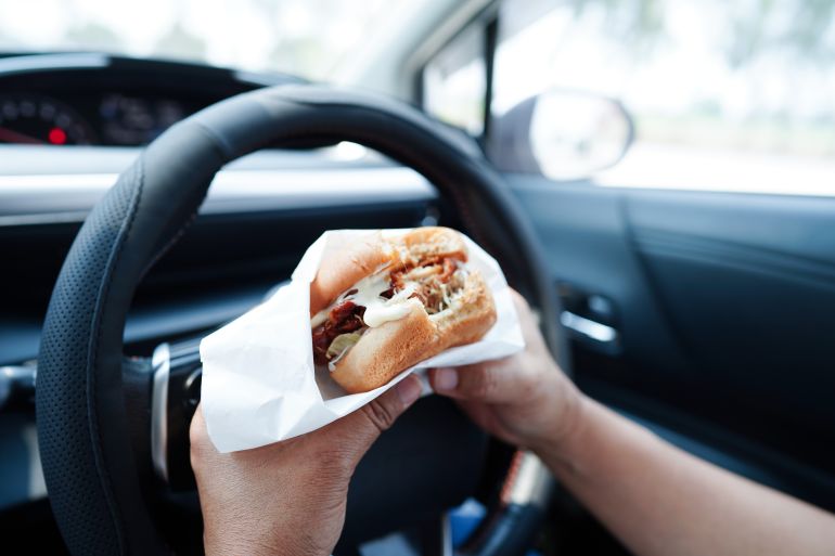 Asian woman driver hold and eat hamburger and french fries in car, dangerous and risk an accident.