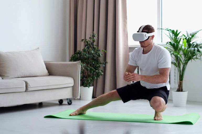 young man in sports clothing doing squat while wearing virtual reality glasses. Training Via Augmented Reality Application, Futuristic Fitness, Smart Sport And Technology Concept; Shutterstock ID 2159672413; purchase_order: aljazeera ; job: ; client: ; other: