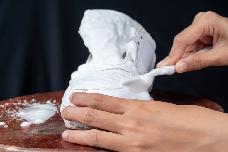 Woman cleaning white leather shoes with cleaning foam. The concept of caring for leather footwear